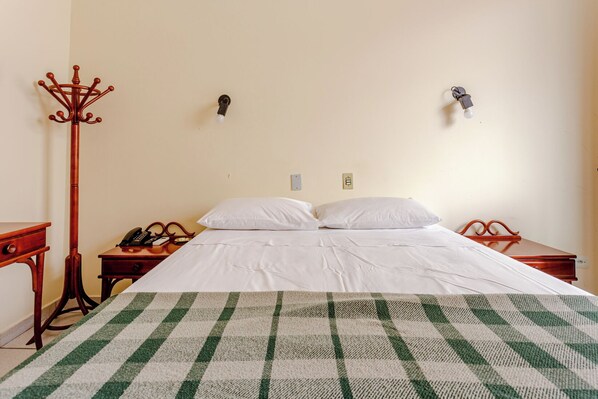 A hotel room with a bed, a telephone, a coat stand, and two wall-mounted light switches. - Daher Center Hotel (São Paulo)