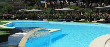 Una piscina al aire libre, sombrillas, sillones reclinables de piscina