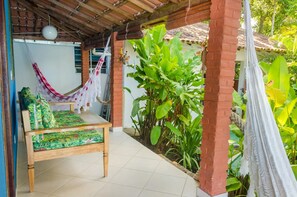 A covered patio with a wooden bench and hammock, surrounded by lush greenery and a tiled floor. - Pousada do Mineiro (Porto Seguro)