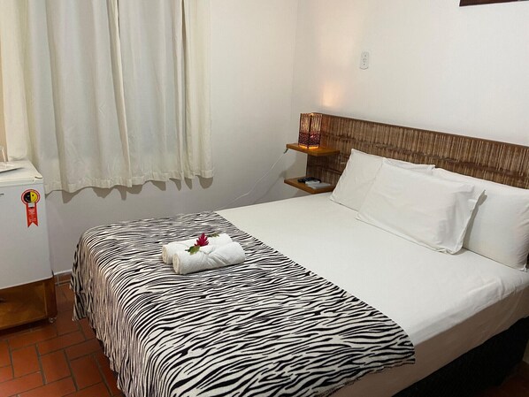 A hotel room with a zebra-striped bedspread, a neatly made bed with white pillows, a bedside table with a lamp, and a window with curtains. - Pousada do Mineiro (Porto Seguro)