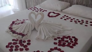 Een bed met witte lakens en rozenblaadjes gerangschikt in hartjes.