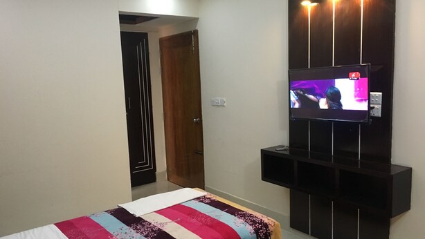 A modern bedroom with a bed, a TV mounted on the wall, and a door leading to another room. - Uttara Suite At Dhaka (Dhaka)