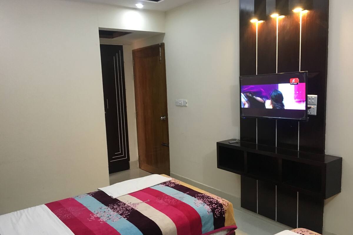 Ein modernes Schlafzimmer mit einem Bett, einem an der Wand montierten Fernseher und einer Tür zu einem anderen Raum.