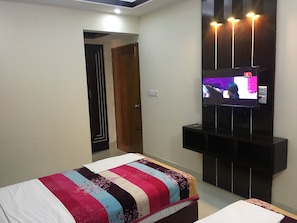 A modern bedroom with a bed, a TV mounted on the wall, and a door leading to another room.