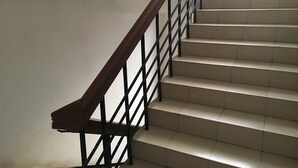 A staircase with a wooden handrail and black metal balusters, leading to an upper floor. - Uttara Suite At Dhaka (Dhaka)