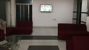 A living room with red sofas, a glass coffee table, a flat-screen TV mounted on the wall, and ceiling fans. - Uttara Suite At Dhaka (Dhaka)