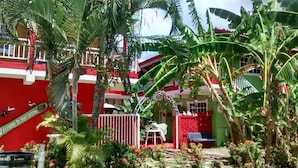 A red and white building with a garden and palm trees. - Posada Nativa Licy (San Andrés)