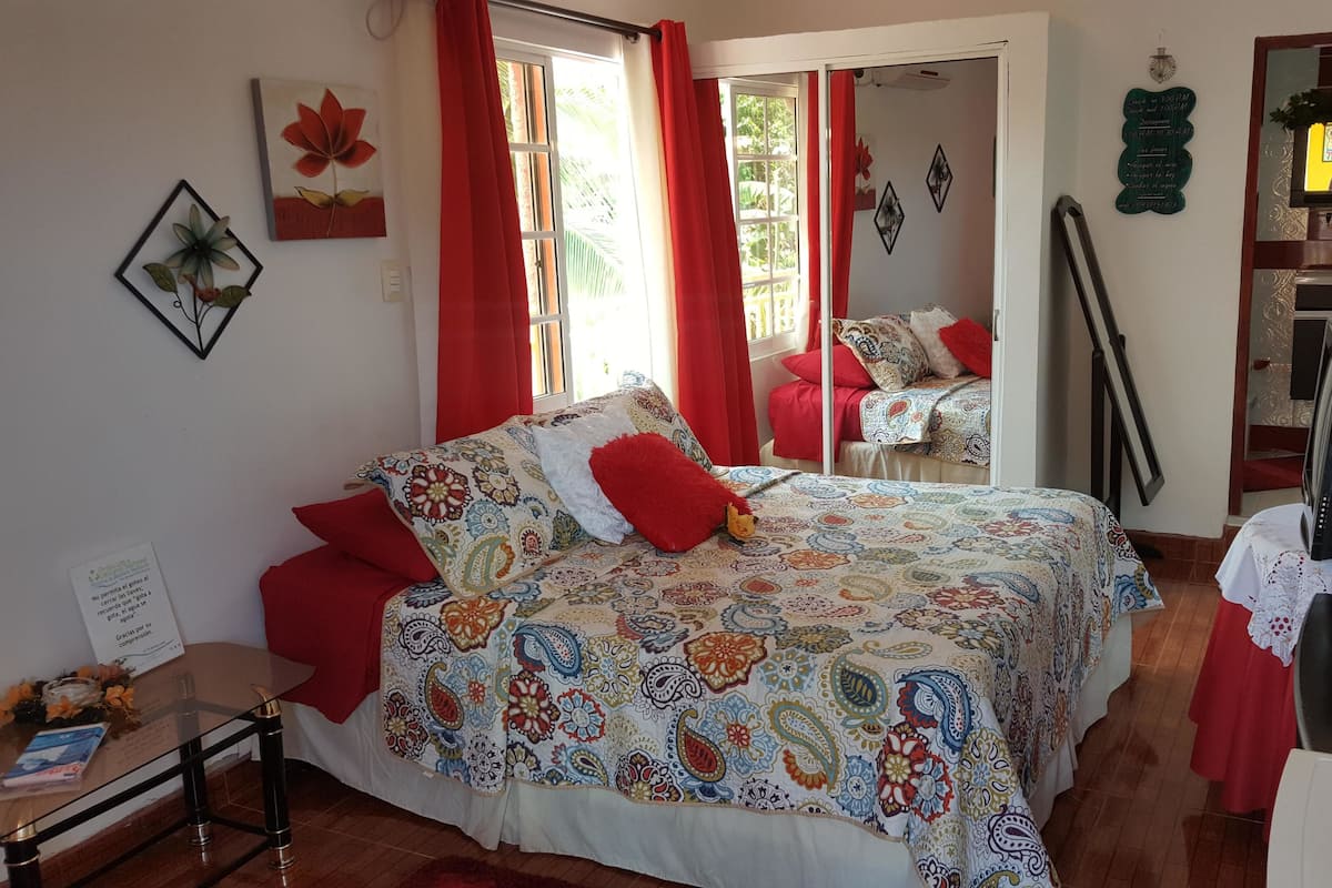 A bedroom with a large bed, red curtains, a TV, and a mirror.