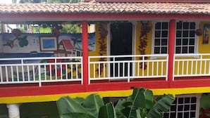 A colorful building with a red and yellow facade, white railings, and a mural depicting tropical scenery. - Posada Nativa Licy (San Andrés)