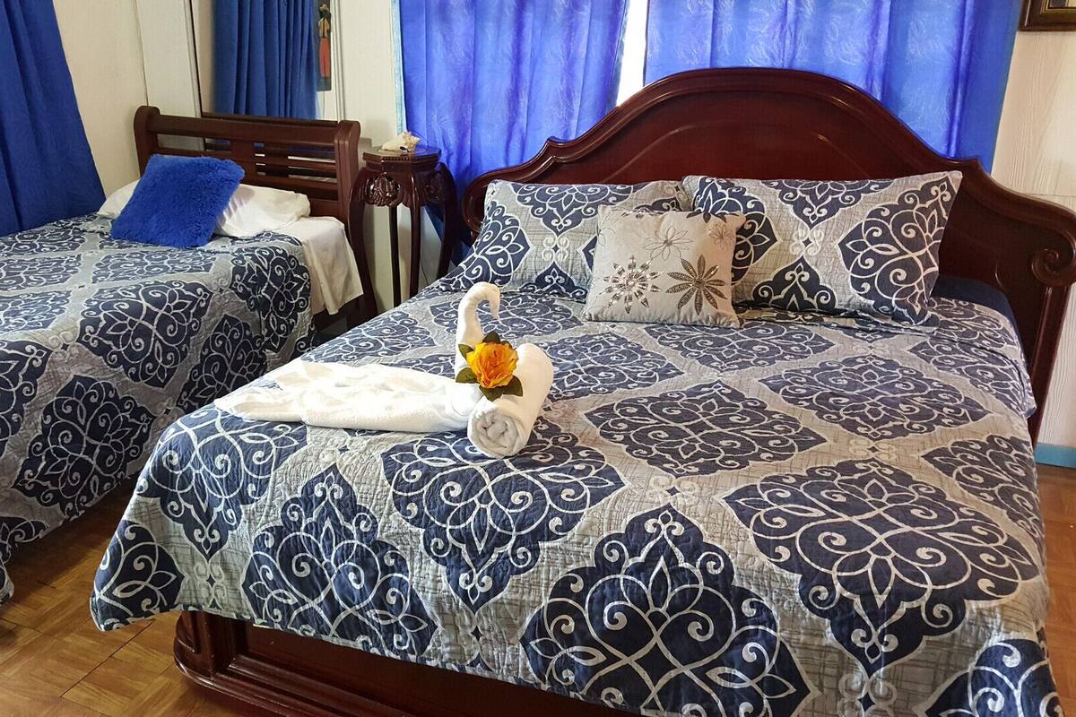 Two double beds with matching blue and white patterned bedspreads, a wooden headboard, and a blue curtain in the background.