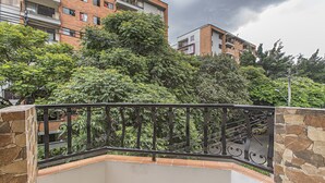 A balcony with a stone wall and metal railing, overlooking a residential area with brick buildings and trees. - Zojo Island (Medellín)