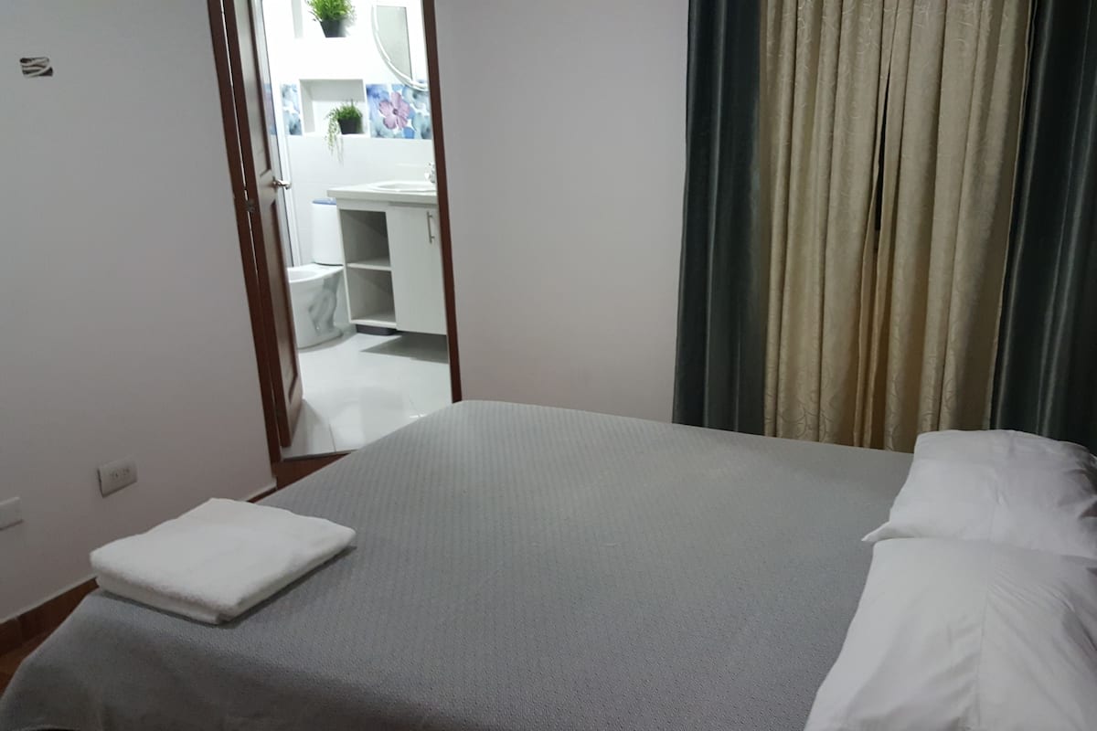 A neatly made bed with white linens, a wooden headboard, and a small white towel on the floor beside it.