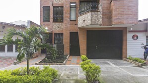 A multi-story residential building with a garage, a balcony, and a small garden area with plants. - Zojo Island (Medellín)