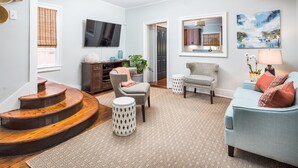 A living room with a TV, a sofa, a chair, a staircase, and a kitchen area visible through an open door. - 69 Spring Street (Charleston)