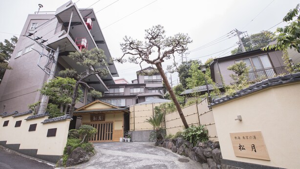 A traditional Japanese building with a sloped roof, a wooden entrance gate, and a stone wall with a sign. - Atami Kinomiyanoyu Shogetsu (Atami)