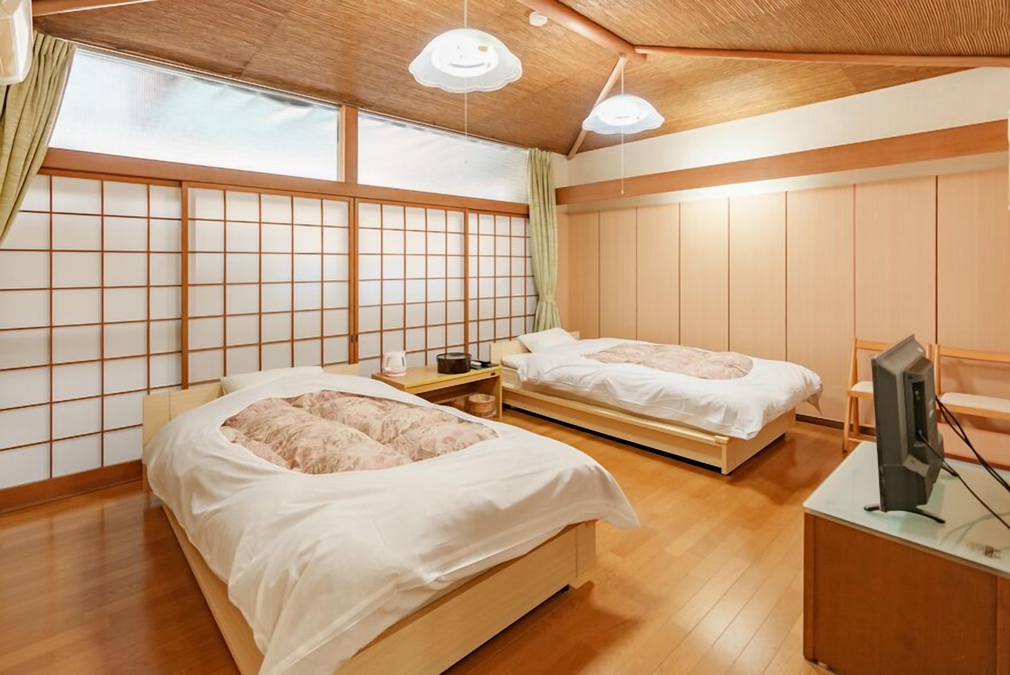 A traditional Japanese-style room with two beds, a TV, and a sliding door.