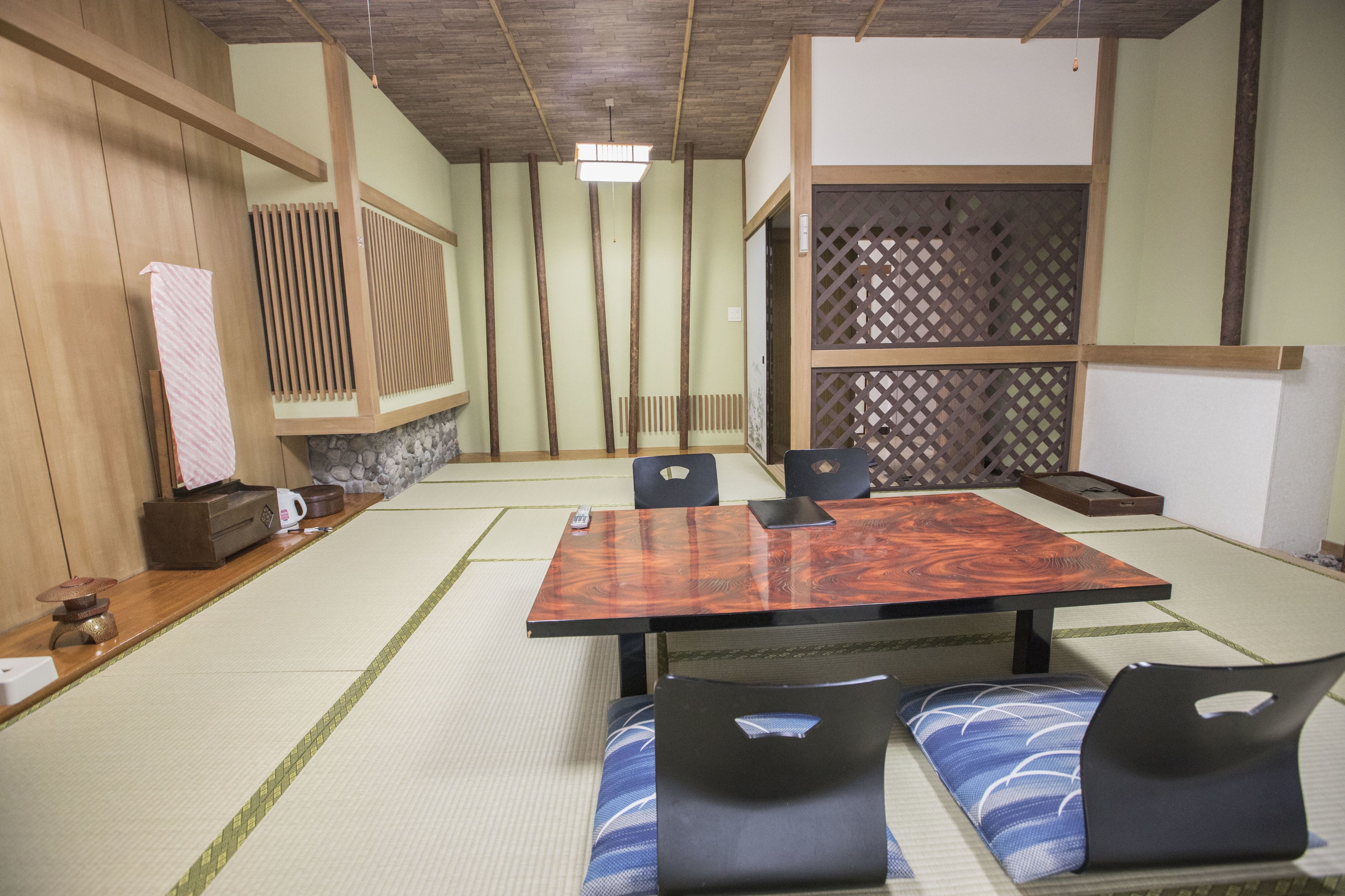 A traditional Japanese room with tatami flooring, a low wooden table, and black cushioned chairs.