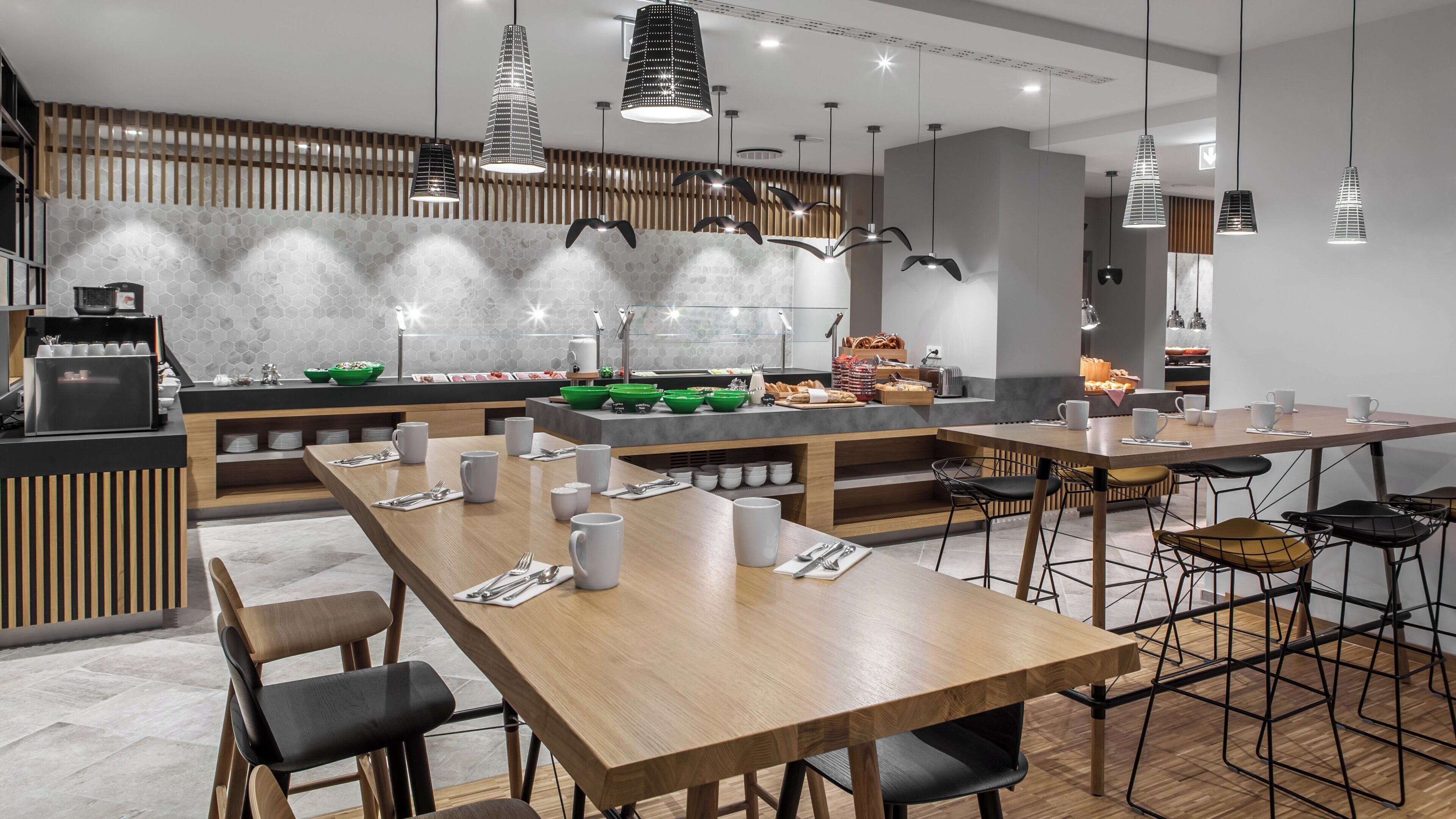 A modern dining area with wooden tables and chairs, a buffet counter, and pendant lighting.
