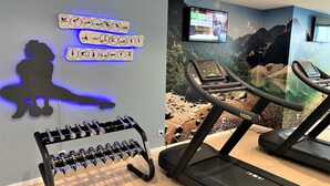 Una palestra con tapis roulant, una TV a parete, una decorazione a silhouette e un porta pesi.