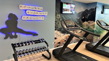 Un gimnasio con cintas de correr, una televisión instalada en la pared, un adorno en silueta y un soporte para mancuernas.