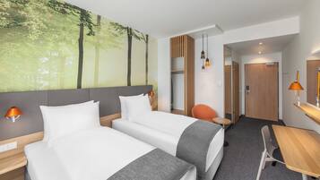 A hotel room with two beds, a desk, a chair, a wardrobe, and a large forest mural on the wall.