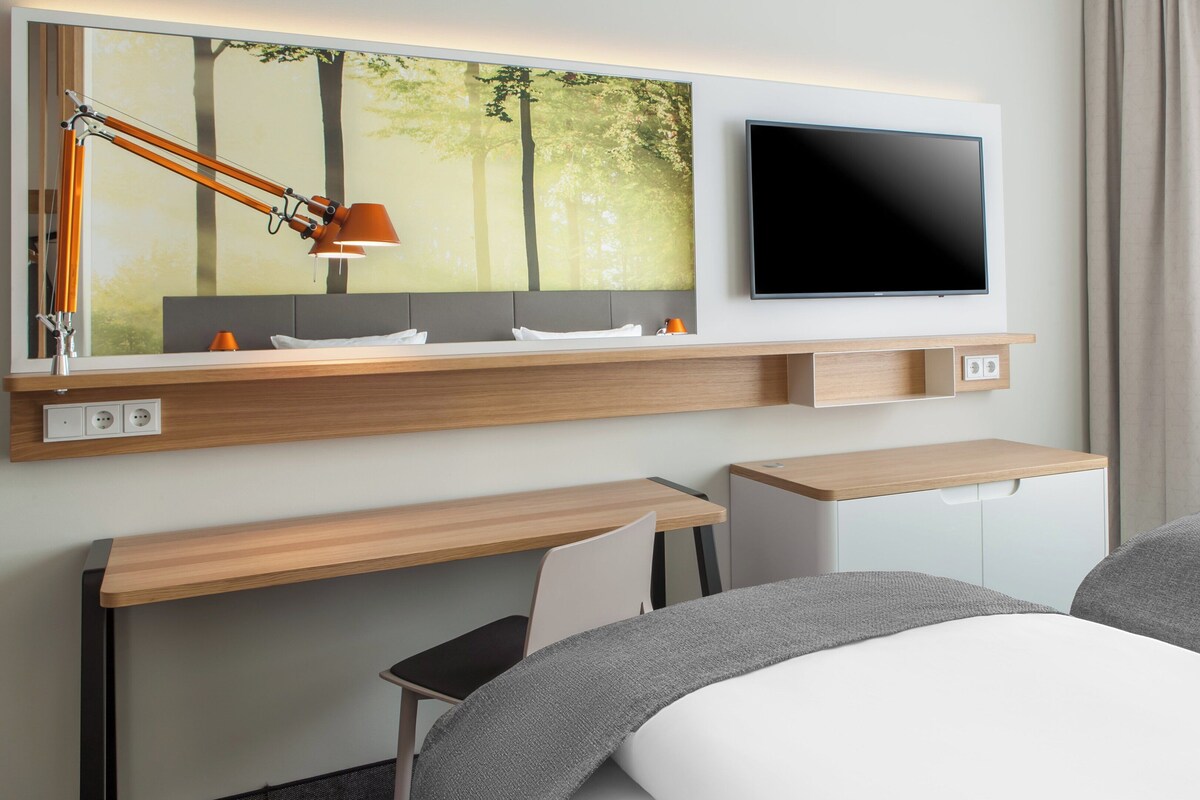 A modern hotel room with a flat-screen TV, a desk, a chair, and a bed.