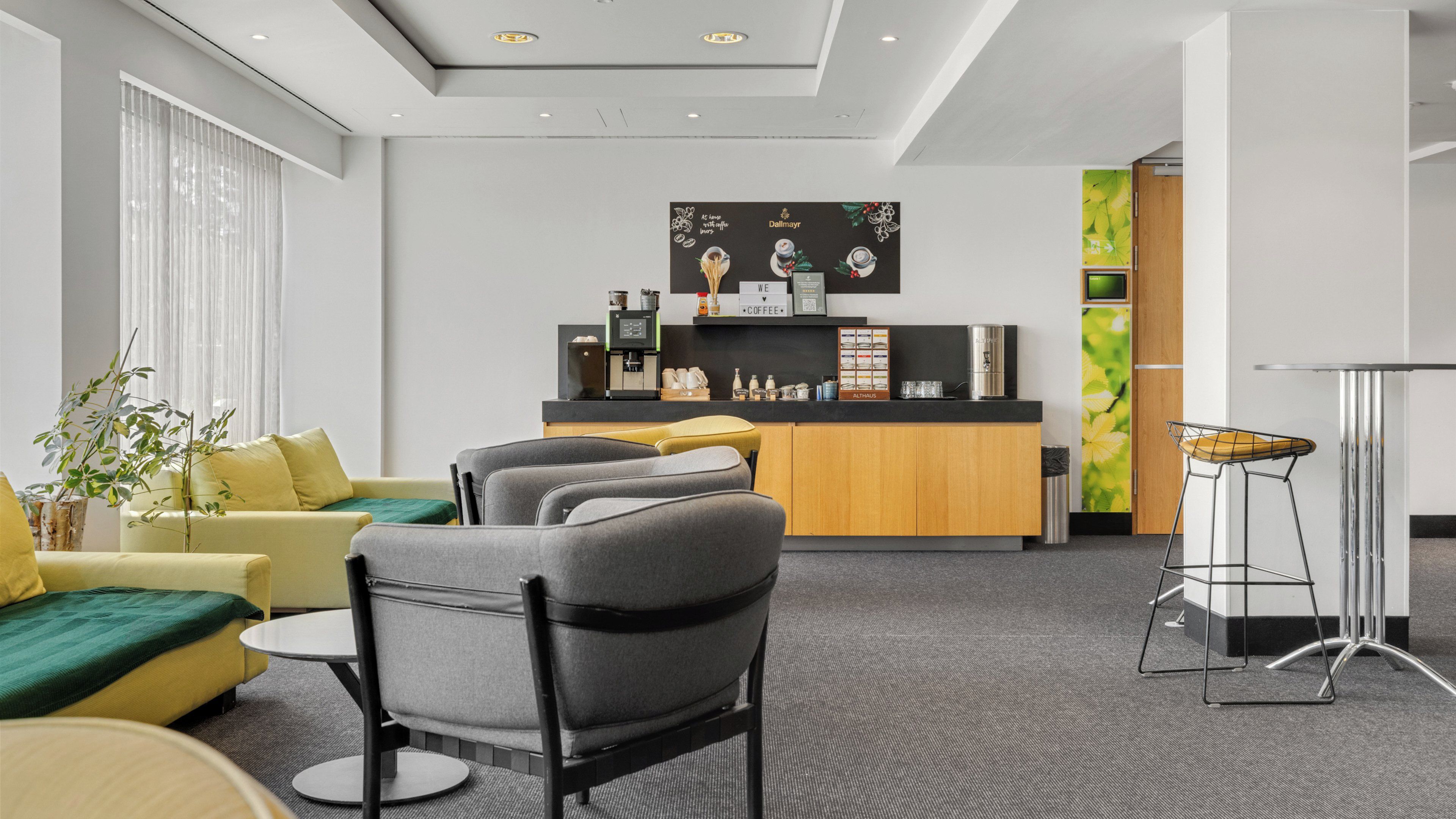 A modern hotel lobby with a reception desk, seating area, and a coffee bar.