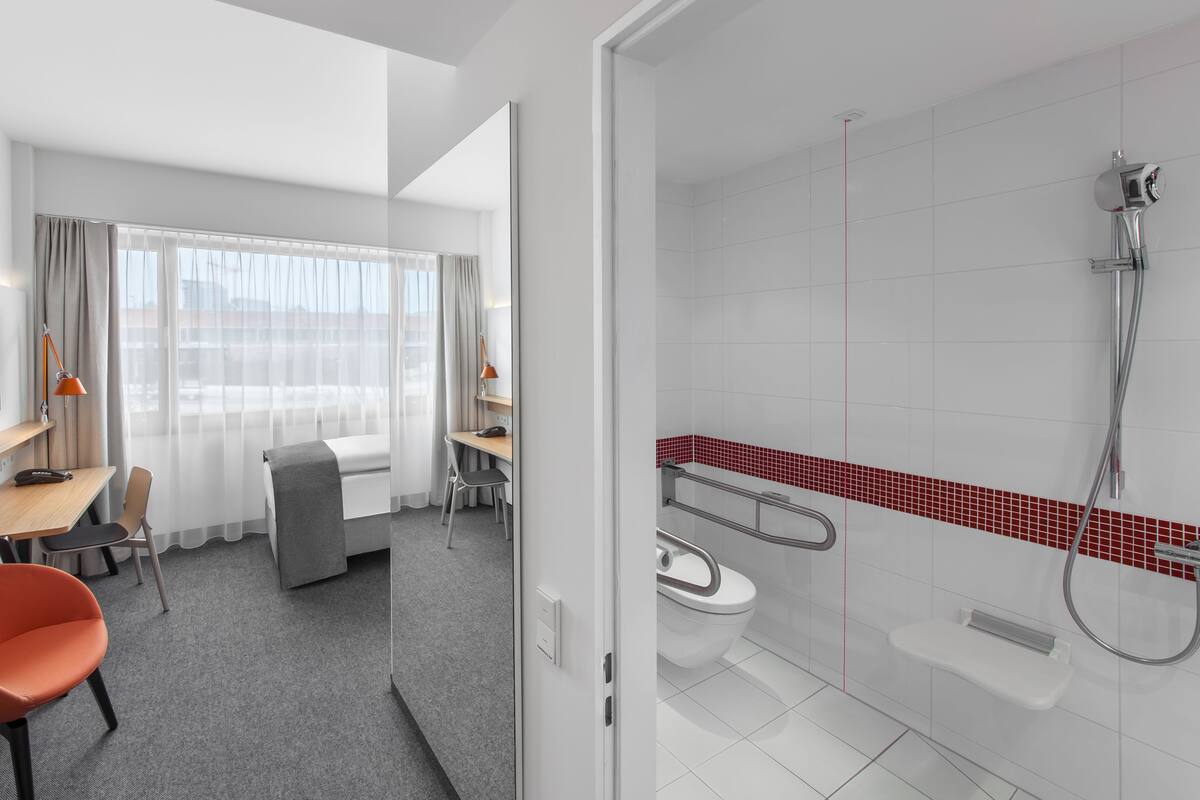 A hotel room with a bed, desk, chair, TV, and a shower area.