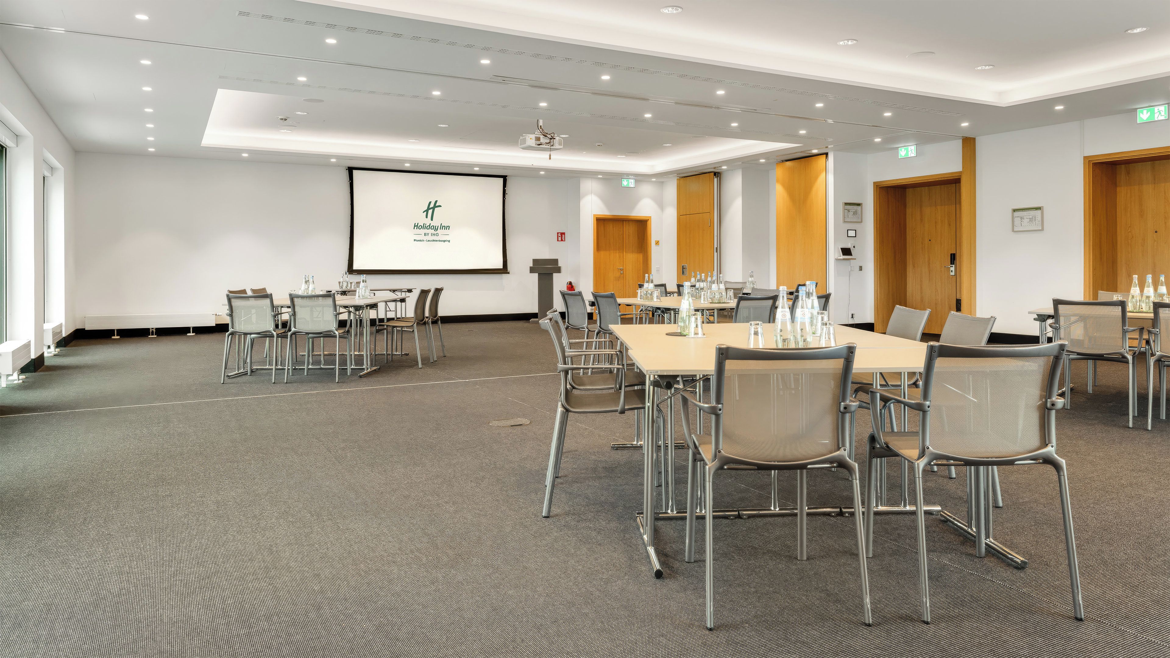 A conference room with tables, chairs, a projector screen, and a presentation.