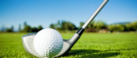 A golf ball on a tee on a grassy field with a golf club in the background.