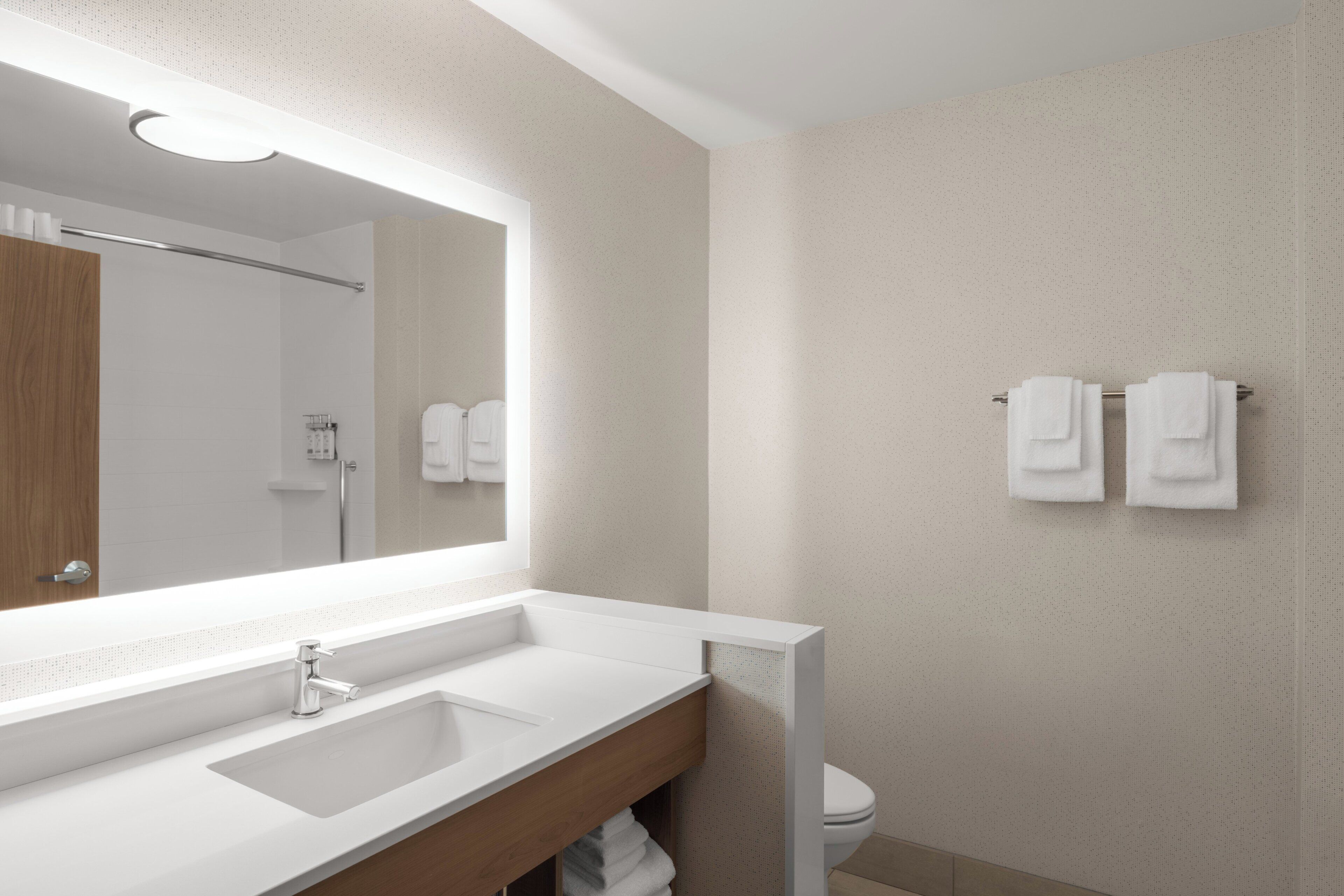 A modern bathroom with a large mirror, a sink, and a toilet.