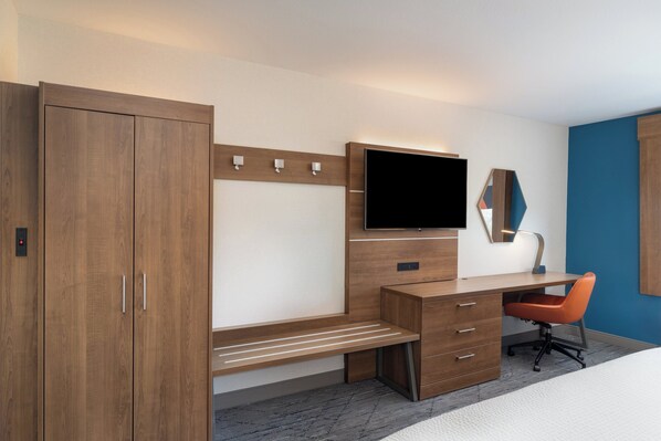Habitación de hotel con un escritorio de madera, un televisor montado en la pared, un espejo y una sola silla naranja.