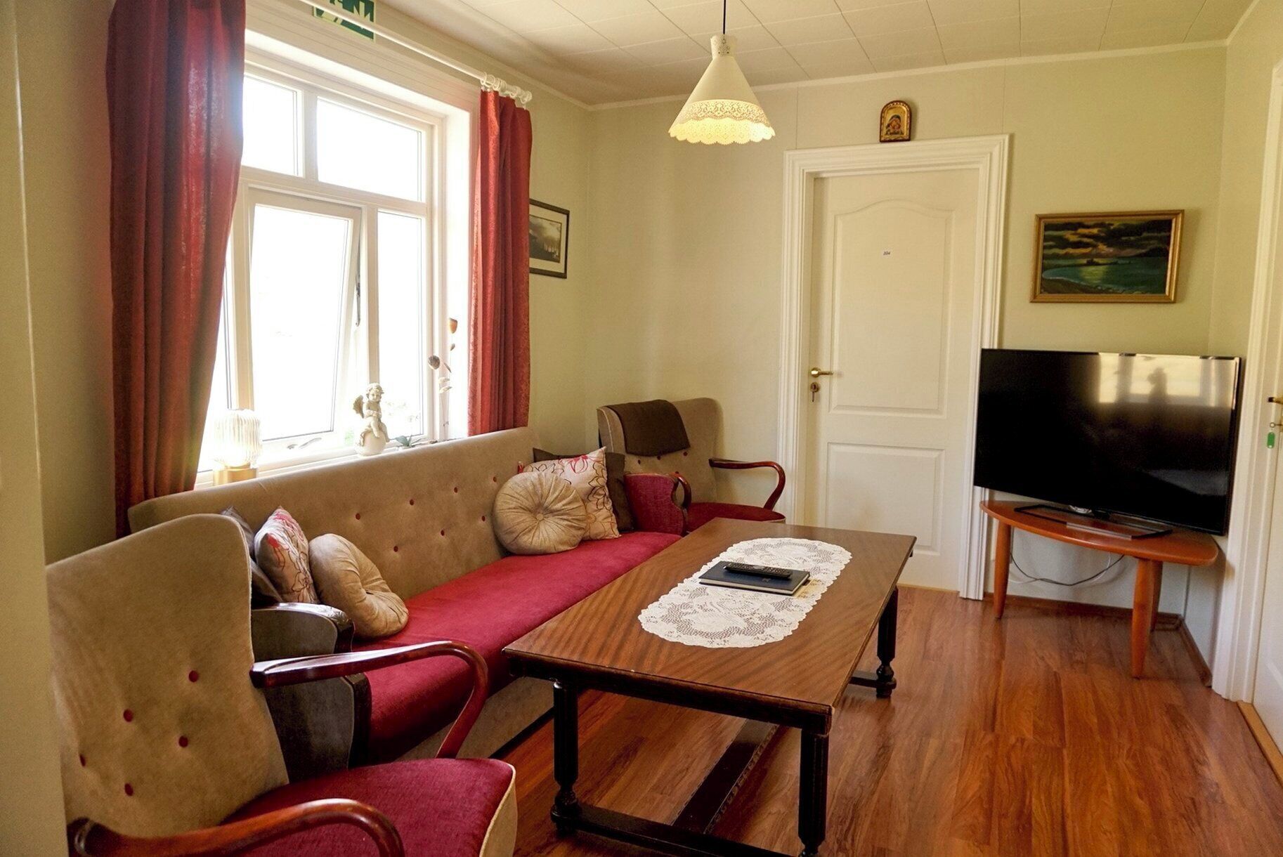 A cozy living room with a sofa, chairs, a wooden coffee table, a television, and a window with curtains.