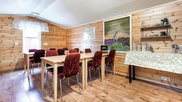 Una habitación con paneles de madera, una mesa de comedor y sillas, un cuadro en la pared y estantes con utensilios de cocina.