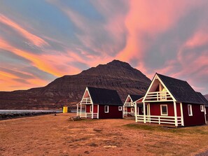 A row of red buildings with white trim and black roofs, set against a backdrop of a mountain and a colorful sky.