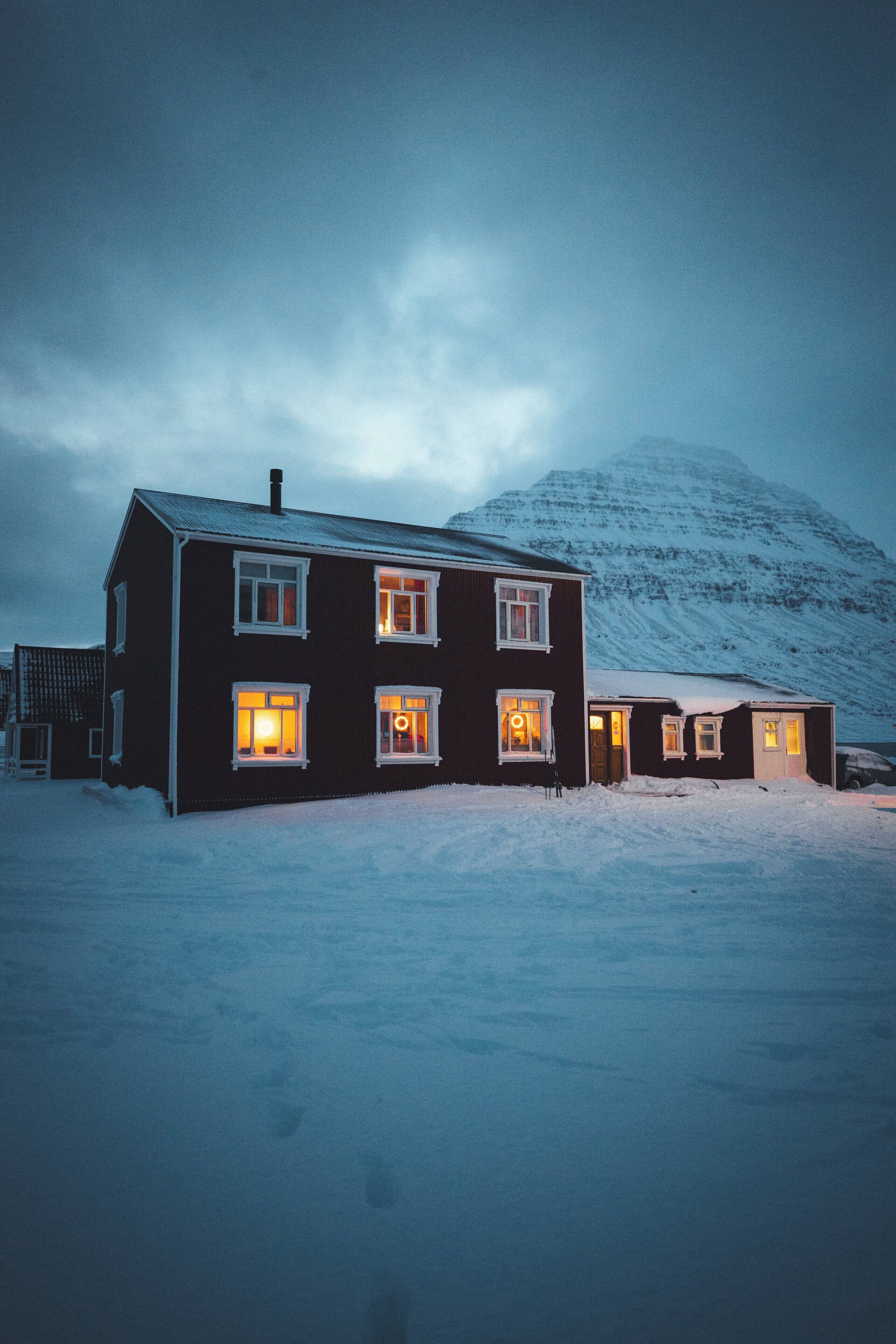 A two-story house with multiple windows and a snow-covered landscape in the background.