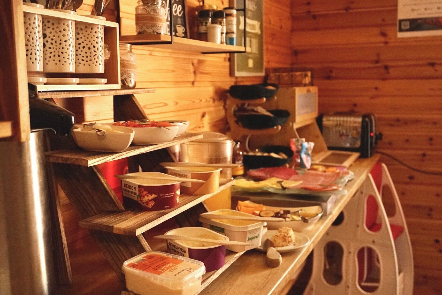 Une cuisine rustique, aménagée dans une cabane en bois, avec des étagères où sont rangés des bocaux, des bols et des récipients.