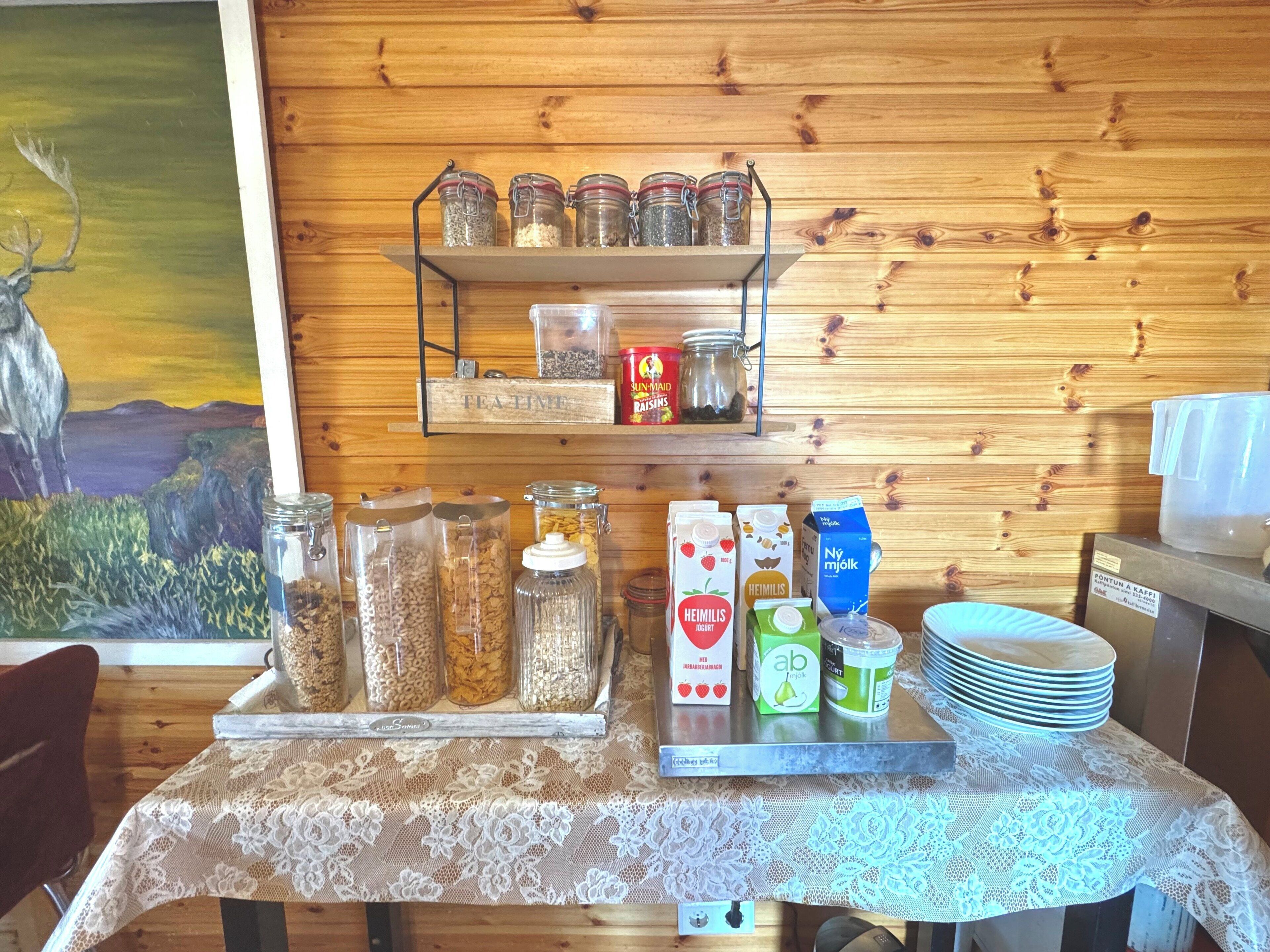 Una mesa de desayuno con diversos alimentos, incluyendo botes de cereal, una caja de pasas y cartones de leche y jugo.