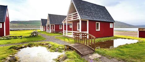 Filas de casas rojas con detalles blancos y techos grises, unidas por un puente de madera sobre un arroyo.