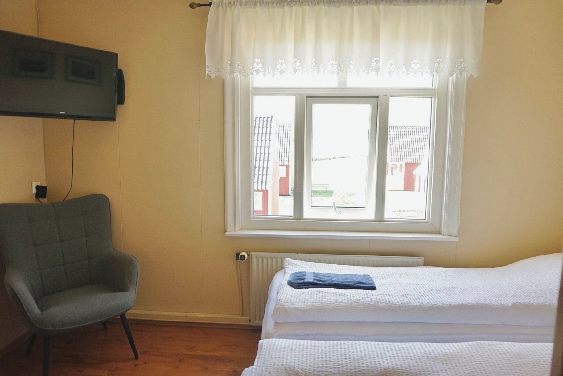 Una habitación con cama, una silla, un ventanal con vistas a edificios y un radiador.
