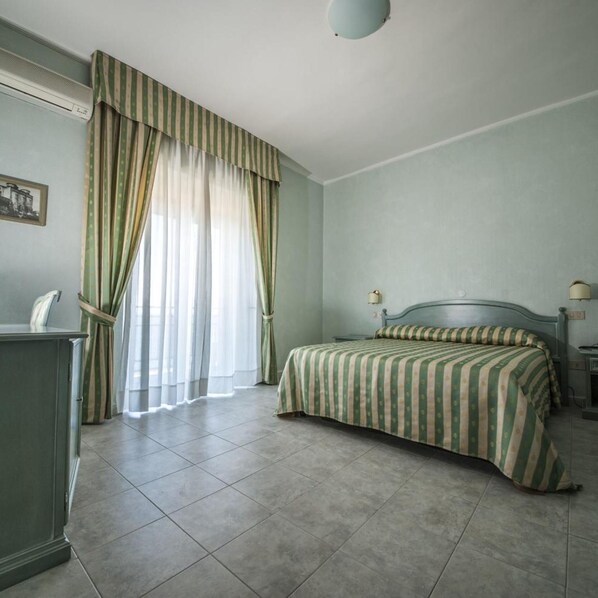 A room with a bed, a desk, a lamp, and a window with curtains.