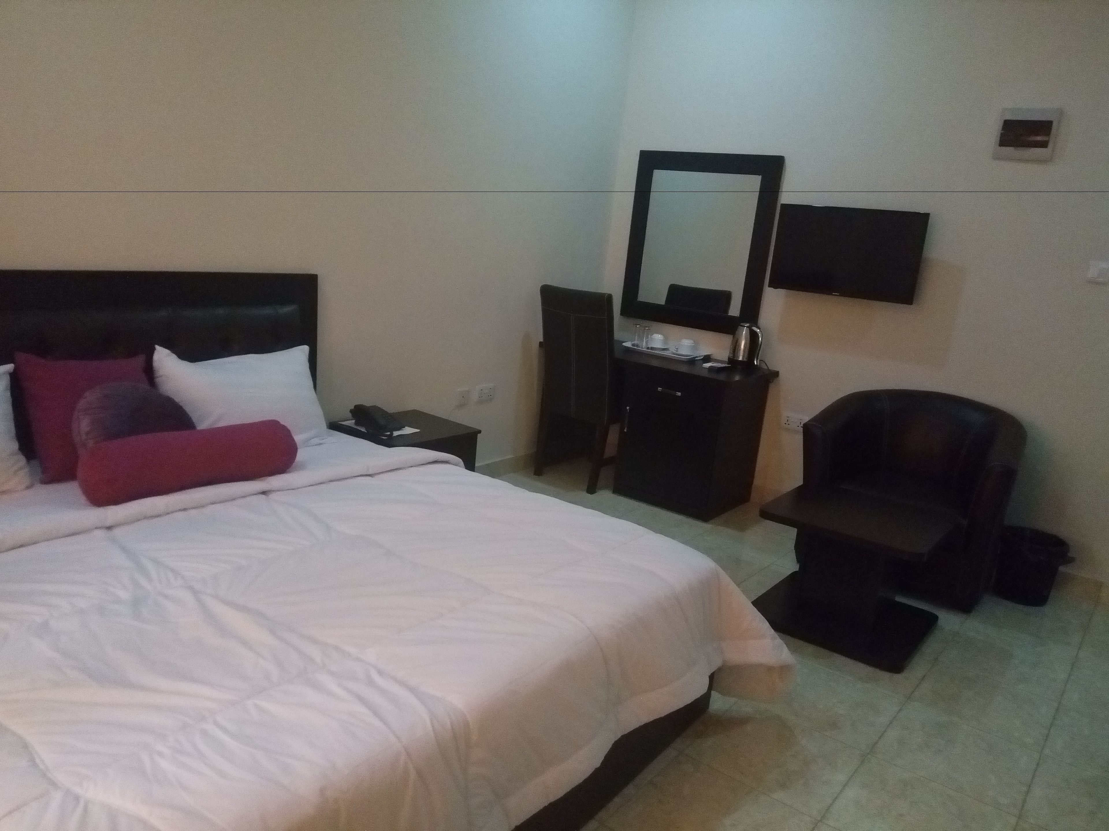 A hotel room with a bed, a desk, a chair, a TV, and a mirror.