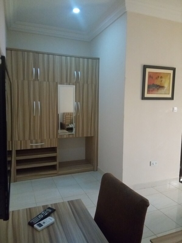 A room with a wooden wardrobe, a mirror, a framed picture on the wall, and a remote control on a table.