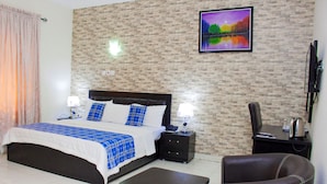 Une chambre d’hôtel avec un lit, des tables de chevet, une télévision, une chaise et un tableau au mur.