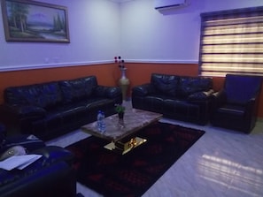 A living room with two black leather sofas, a coffee table, and a vase with flowers. - Peace Media Hotels (Abuja)