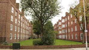 A row of red brick apartment buildings with a green lawn and a tree in the center. - Beechwood House (London)