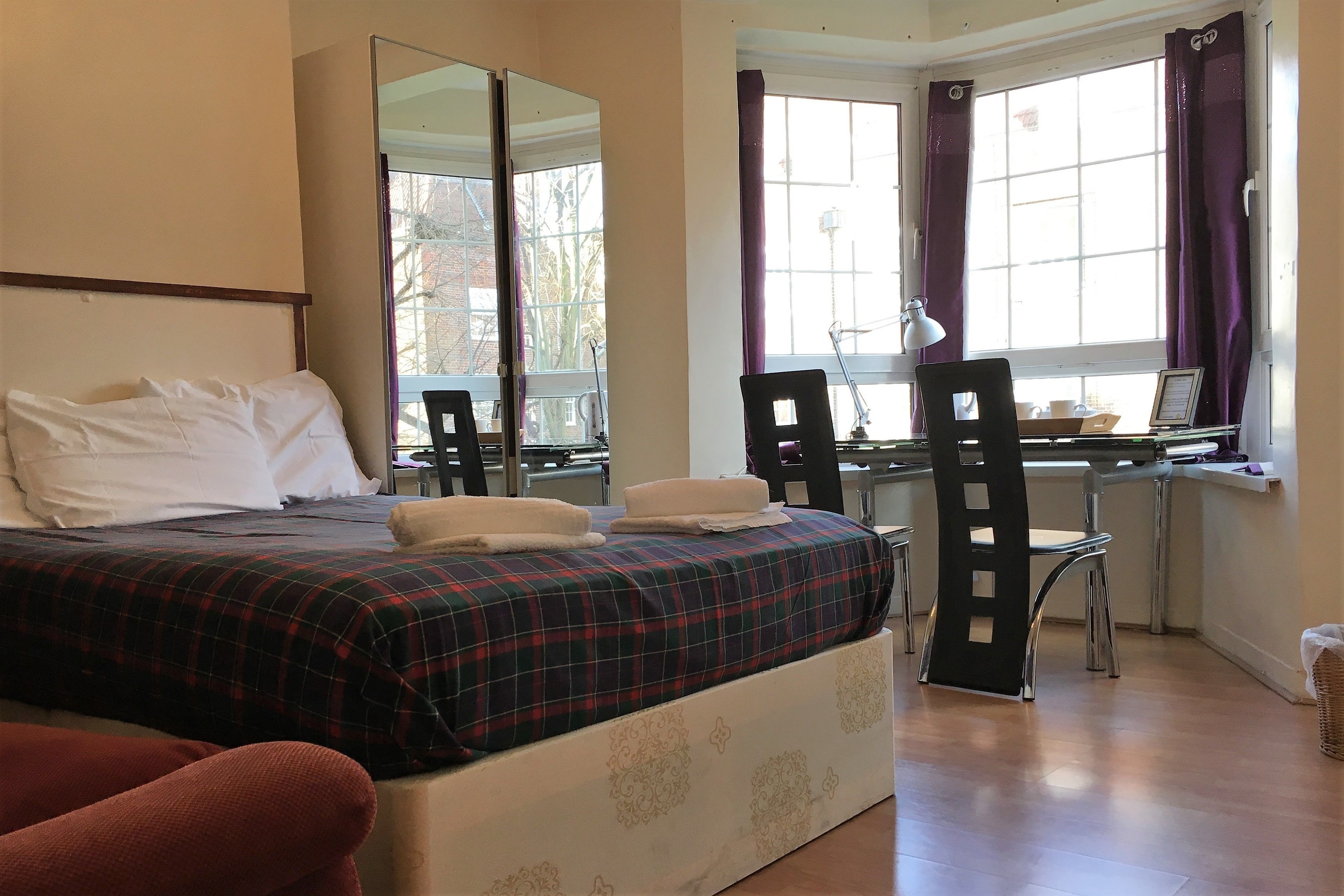 Ein Schlafzimmer mit Bett, Schreibtisch, Stuhl und einem Fenster mit Vorhängen.