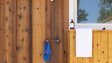 Un mur extérieur en bois avec une fenêtre, une serviette suspendue à un crochet et une bouteille de gel hydroalcoolique.