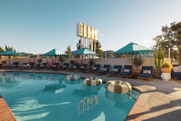 A swimming pool with lounge chairs and umbrellas, surrounded by potted plants and a clear sky.