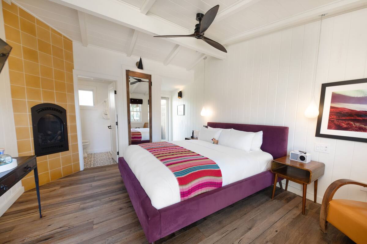 Quarto com uma cama grande, piso de madeira, ventilador de teto e um quadro na parede.